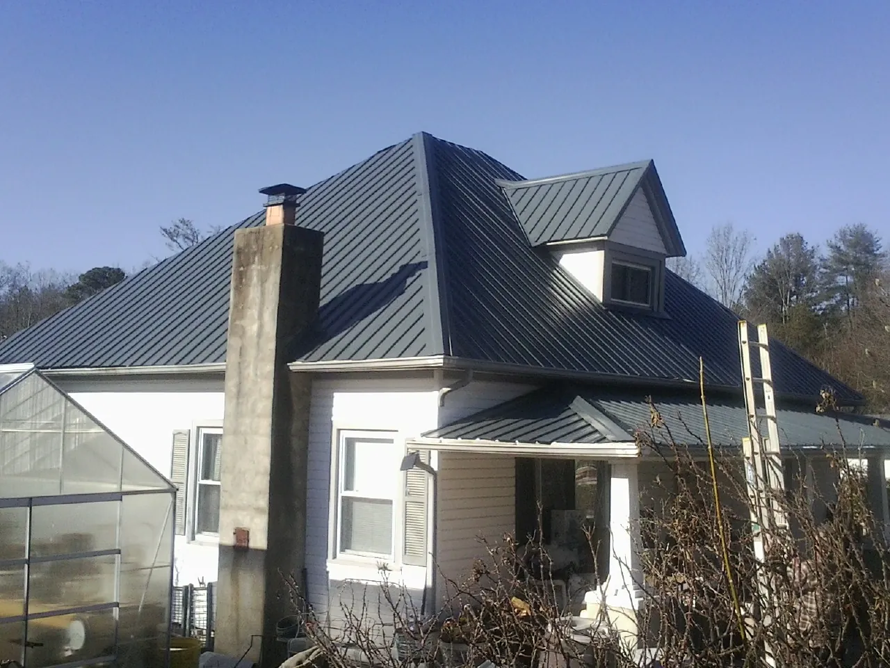 Dark blue standing seam metal roof on a white farmhouse with dormer — Slate & Tile Roof Repair by Roofing Brothers in Ebony