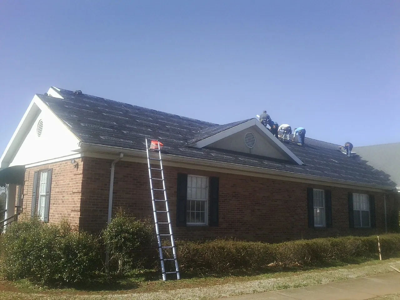 Crew tearing shingles off a brick ranch roof with a ladder set — Emergency Roof Repair work by our crew in Ebony