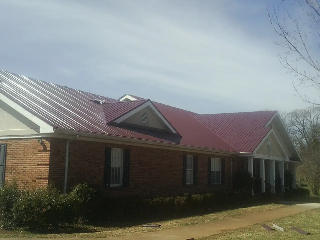 Red metal roof with gabled entries on a long brick building, from a Hail Damage Roof Repair job in Ebony