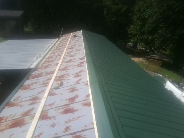 Old rusted panels beside newly installed green metal roofing — Wind Damage Roof Repair by Roofing Brothers in Ebony