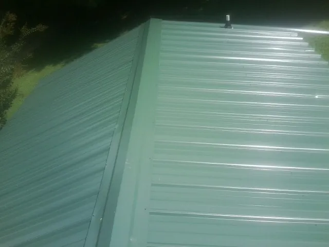 New green metal panels meeting at the ridge of a roof — Flat Roof Repair work by our crew in Ebony