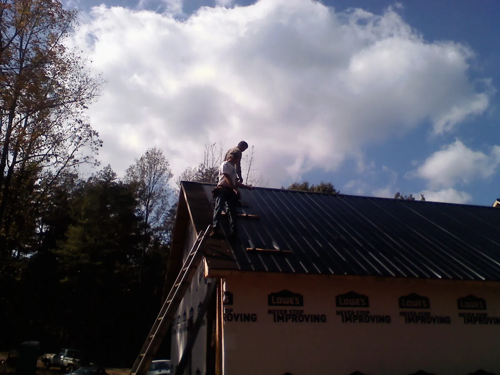 Roofer fastening dark metal panels high against a cloudy sky, from a Roof Inspection job in Ebony