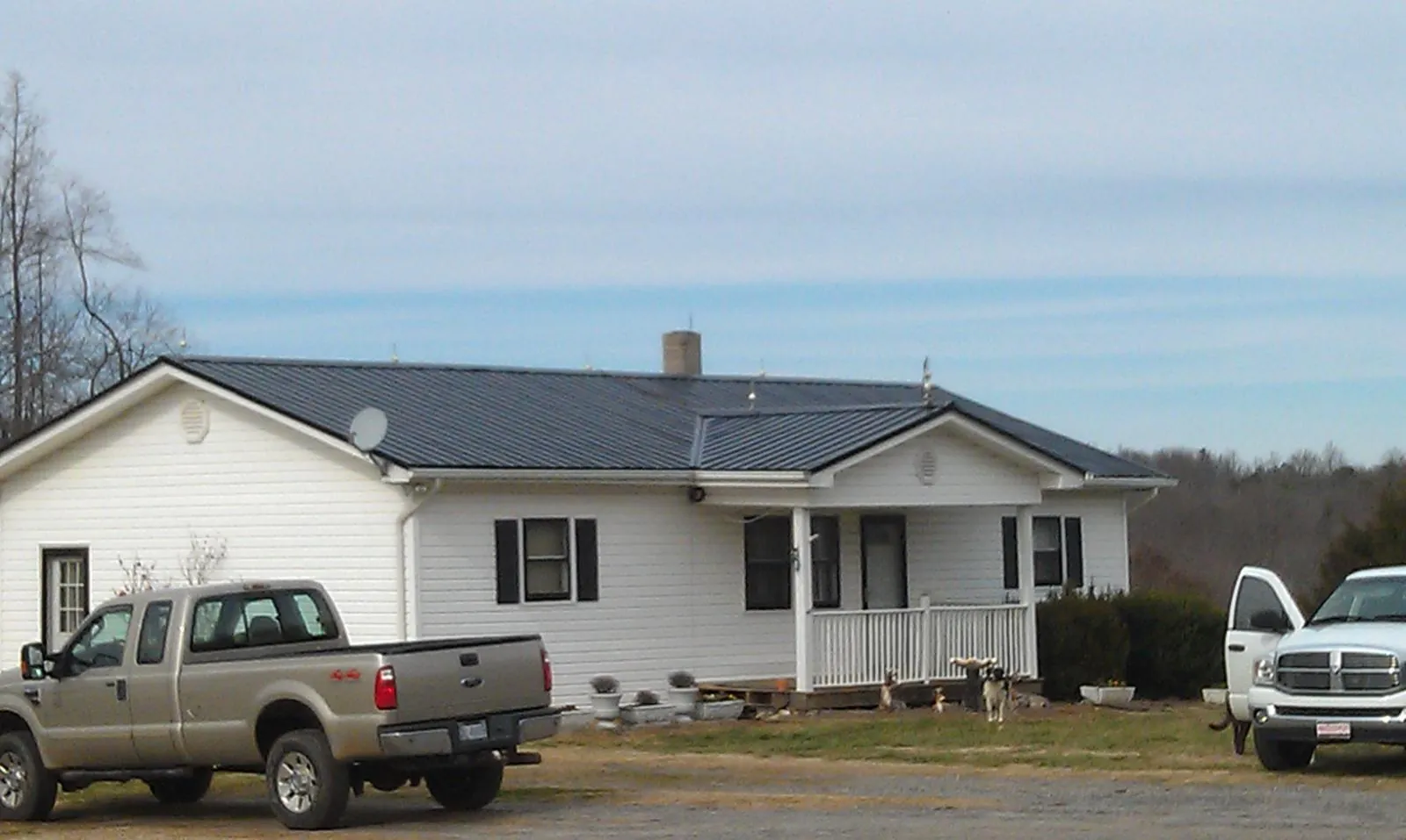 Finished dark metal roof on a white ranch home with work trucks parked in Ebony