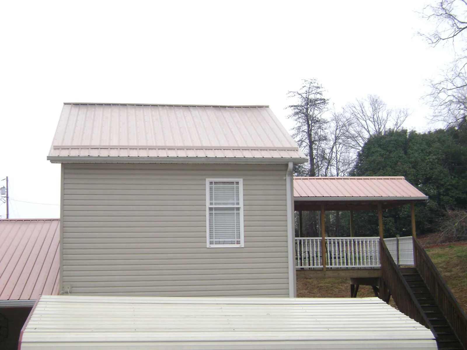 Tan metal roofs on a two story addition and attached porch, from a Roof Replacement job in Ebony
